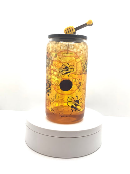 16 oz glass can, snowglobe style. Simple graphic design of bumblebees flying all over,  with one bee hive and sporadic honeycomb design printed on cup surface. Snowglobe wall filled with fixed resin pieces at top to resemble honeycomb and then filled with honey colored glycerin that drips down and settles in bottom. Gives illusion of constant dripping honey. Black acrylic lid and a honey dipper straw topper 
